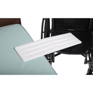 A white transfer board is positioned between a wheelchair and a padded seat, facilitating easy transfer. The wheelchair features black upholstery and armrests. The scene is set in a well-lit room with a neutral background.